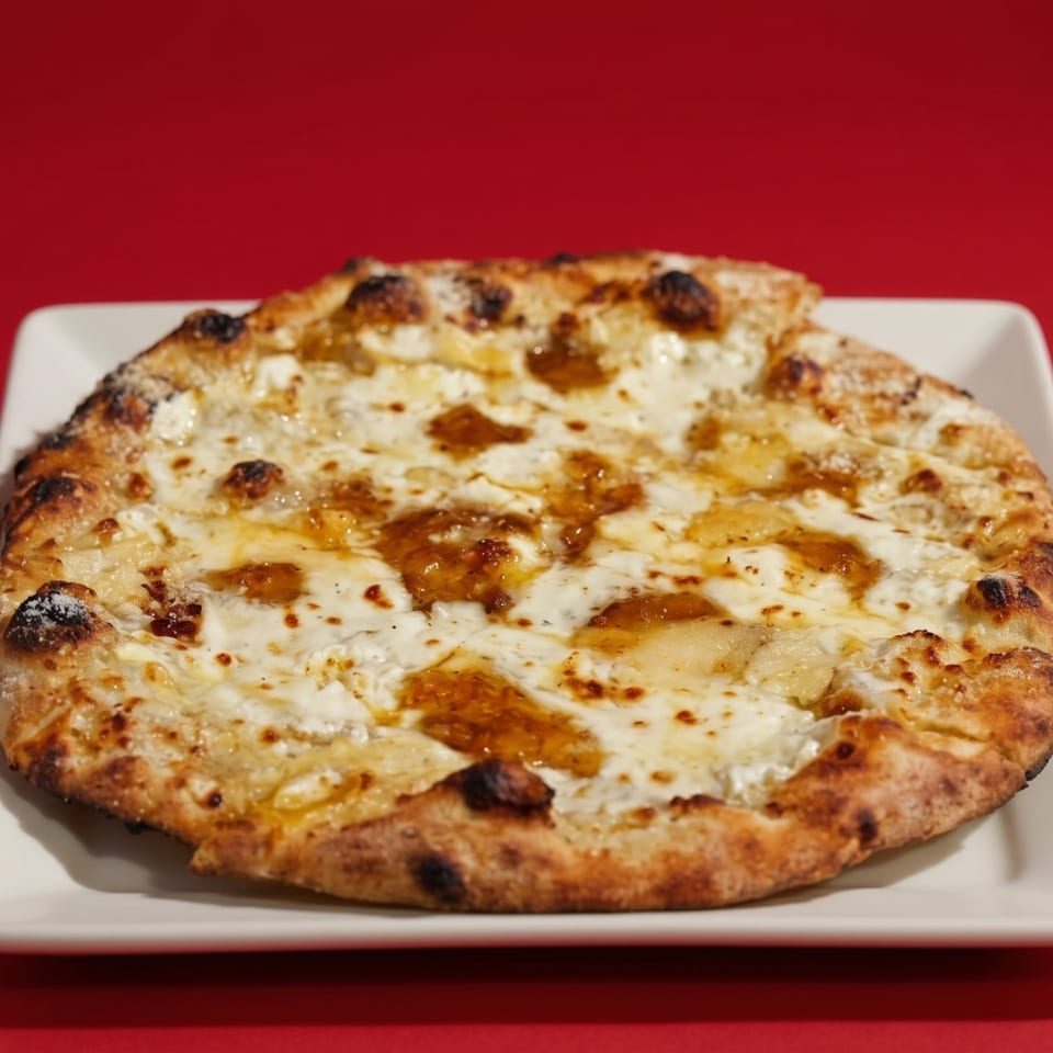 A white cheese pizza with dollops of golden honey on a white plate against a red background.