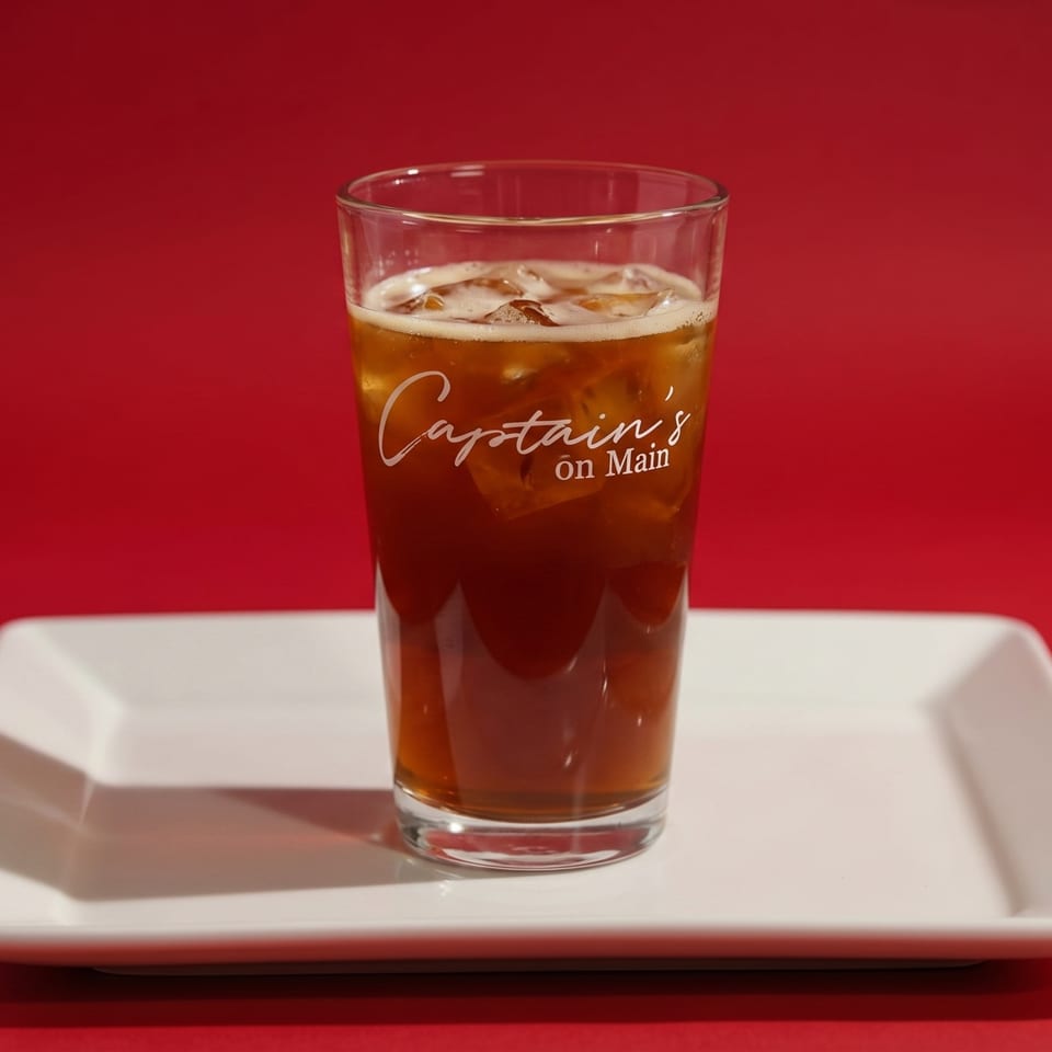Iced tea in a glass with "Captain's on Main" logo, on a white plate against a red background.